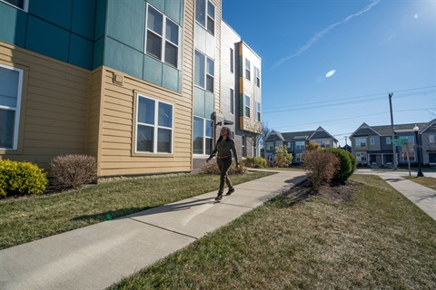 Image of a woman walking on a sidewalk next to an affordable housing community