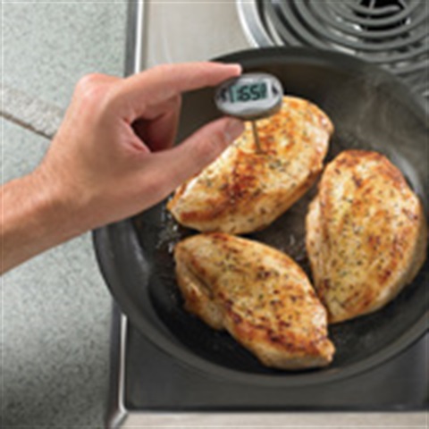 Chicken cooking in a pan with a hand holding a thermometer in one of the pieces that reads 165°F